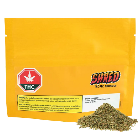 Front-facing yellow pouch with a small pile of loose herb at the lower right and "Tropic Thunder" logo visible on the front.