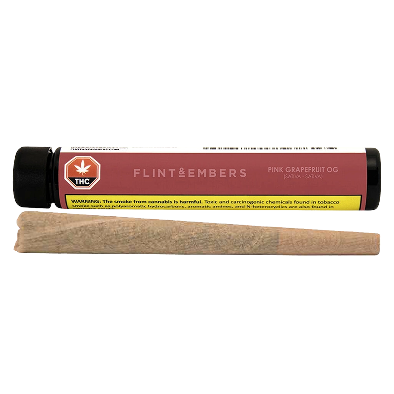 Horizontal studio shot of a rolled joint in front of a pink-labeled Flint & Embers Pink Grapefruit OG PR 1 x 1 g tube, showing the warning label.