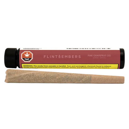 Horizontal studio shot of a rolled joint in front of a pink-labeled Flint & Embers Pink Grapefruit OG PR 1 x 1 g tube, showing the warning label.