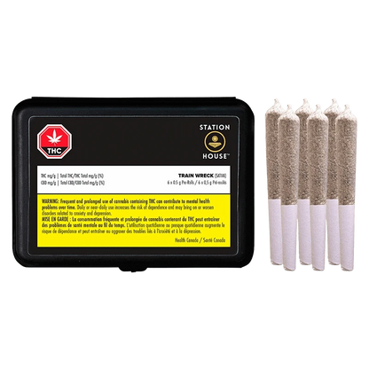 Right-side view of five rolled pre-rolls next to a black tin labeled "Trainwreck PR 6 x 0.5 g" showing warning text and Station House branding.