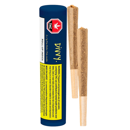 Vertical studio shot of a blue Divvy Roll Up Indica PR 2 x 1 g tube beside two pre-rolled joints on a white background