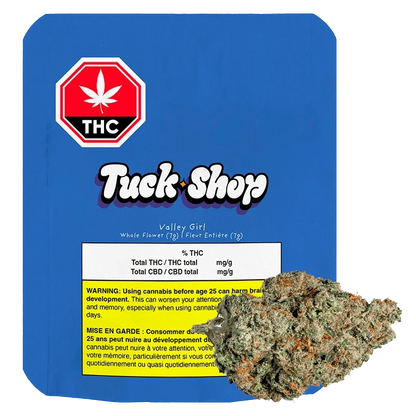 Front-facing shot of the Tuck Shop Valley Girl 7 g package on blue backing with a cannabis bud overlapping the lower right.