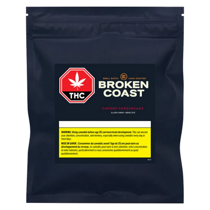 Front-facing shot of the navy resealable pouch labeled "Broken Coast Cherry Cheesecake" with a prominent red THC symbol and yellow warning panel.