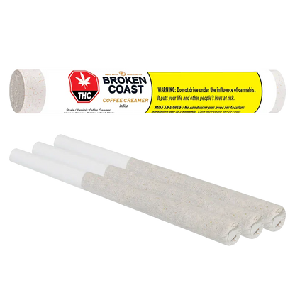 Angled close-up of three rolled joints below a horizontal Broken Coast Coffee Creamer PR 3 x 0.5 g tube with bold yellow warning label.