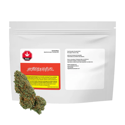 Front-facing, studio-lit image of a white resealable pouch labeled "Cement Shoes" by Snicklefritz with two green cannabis buds placed at the lower left.