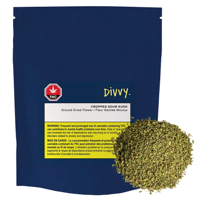 Front-facing navy pouch labeled "Divvy. Cropped Sour Kush" with a white and yellow warning panel and a loose 7 g mound of green dried flower at the lower right