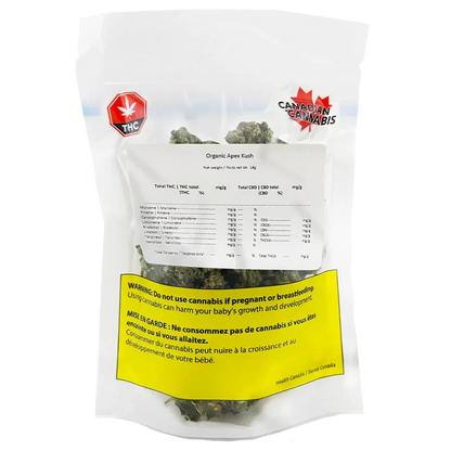 Clear front-facing shot of a sealed bag labeled Organic Apex Kush showing cannabis buds through the pouch and a prominent yellow health warning.