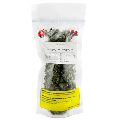 Clear front-facing view of a sealed bag of Organic Apex Kush showing dense green buds, a white label of contents, and a yellow warning panel.