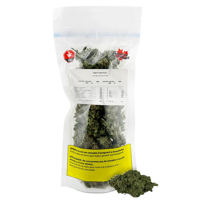 Front-facing shot of a clear resealable bag of Organic Apex Kush showing green buds inside, label text and a yellow warning panel.