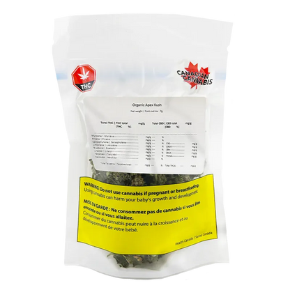 Front-facing shot of a clear pouch labeled Organic Apex Kush showing dried buds through the window, white label details, and a yellow health warning.