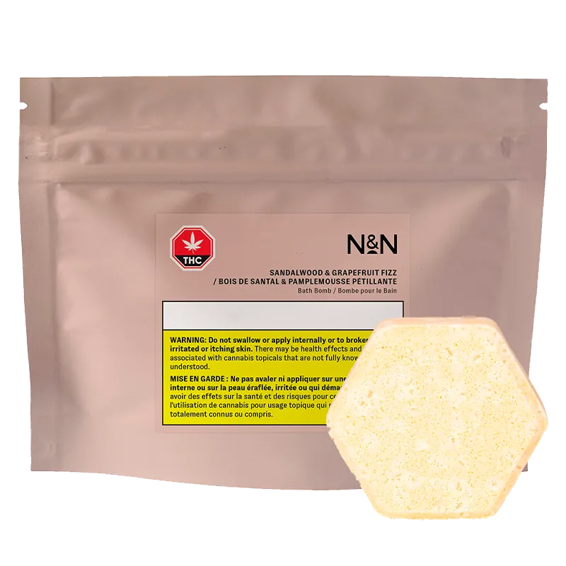 Front-facing pouch labeled N&N Sandalwood & Grapefruit Fizz Bath Bomb with a pale yellow hexagonal bath bomb resting at the lower right.