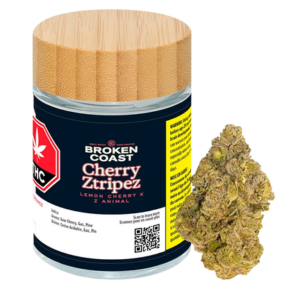 Front-facing jar with a wood-grain lid and a loose bud beside it labeled "Broken Coast Cherry Ztripez" on a dark navy label.