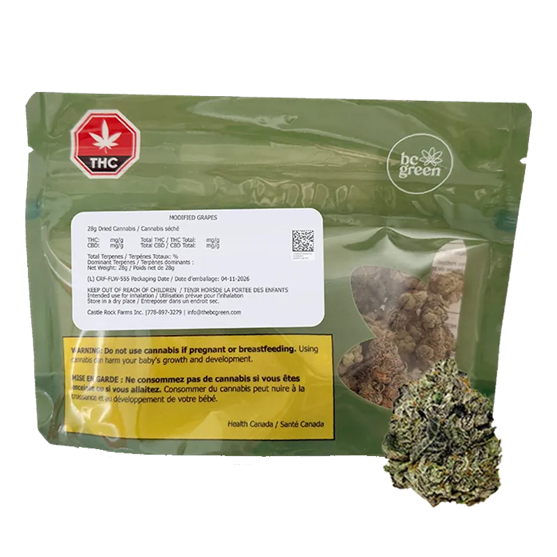 Rear view of a green bc green Modified Grapes pouch with a white info label, yellow warning panel, and visible cannabis buds through a clear window.