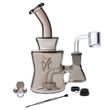 Angled close-up of the Dab Freak - Tsunami Dab Rig 6.5 in in smoky glass, shown with its bent mouthpiece, side banger, logo on the body, and accessories laid out.