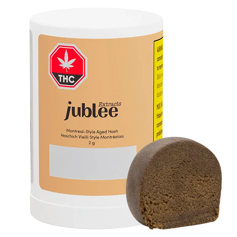 Front-facing shot of the Jubilee Extracts Montreal-Style Aged Hash 2 g cylinder with a brown half-disc of hash leaning against it.