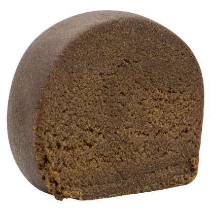 Close-up front view of a dense, dark brown half-cylinder of Montreal-Style Aged Hash showing its crumbly, textured interior.