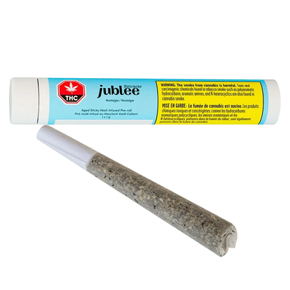 Close-up of a rolled joint in front of a horizontal blue and yellow tube labeled "Nostalgia - Aged Sticky Hash Infused PR 1 x 1 g" by jublee.