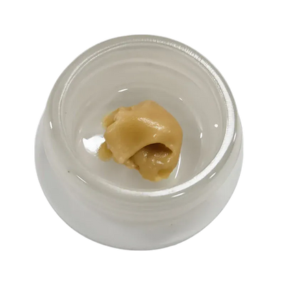 Top-down view of a pale gold dab of Mango Mac Live Rosin resting in the center of a small white glass jar.