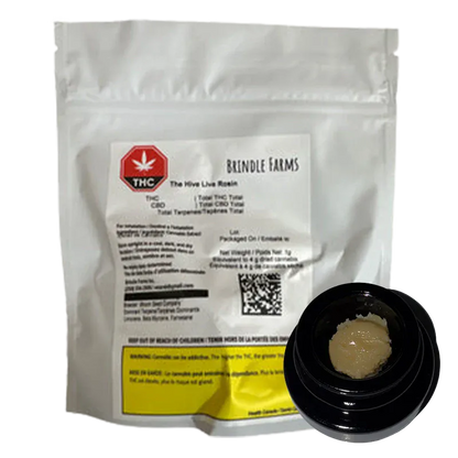 White pouch with a printed label and a small black jar showing pale, crumbly concentrate in the foreground of The Hive Live Rosin image.