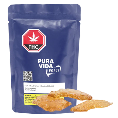 Front-facing view of a blue resealable pouch labeled Pura Vida Legacy with three amber slabs of Slap & Tickle Jumbo Slab Shatter arranged at its base