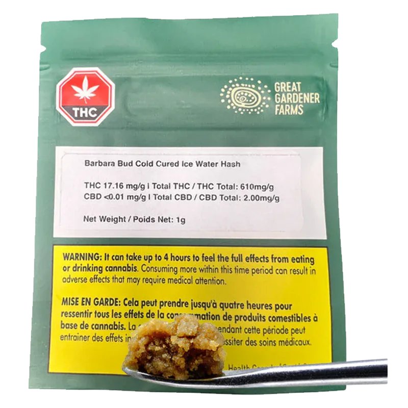 Close-up of a metal scoop holding a golden nugget of concentrate in front of a green pouch labeled Barbara Bud Cold Cured Ice Water Hash.