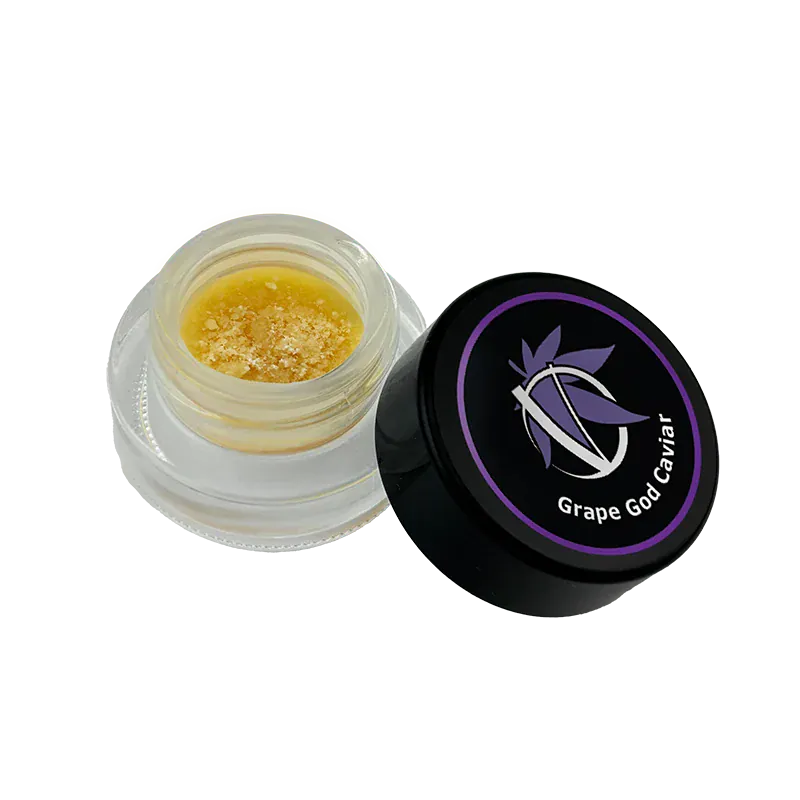 Angled top view of an open jar showing golden crumble beside the black lid labeled Grape God Caviar.