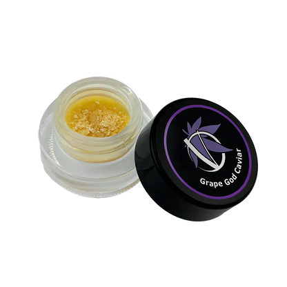 Angled top view of an open jar showing golden crumble beside the black lid labeled Grape God Caviar.