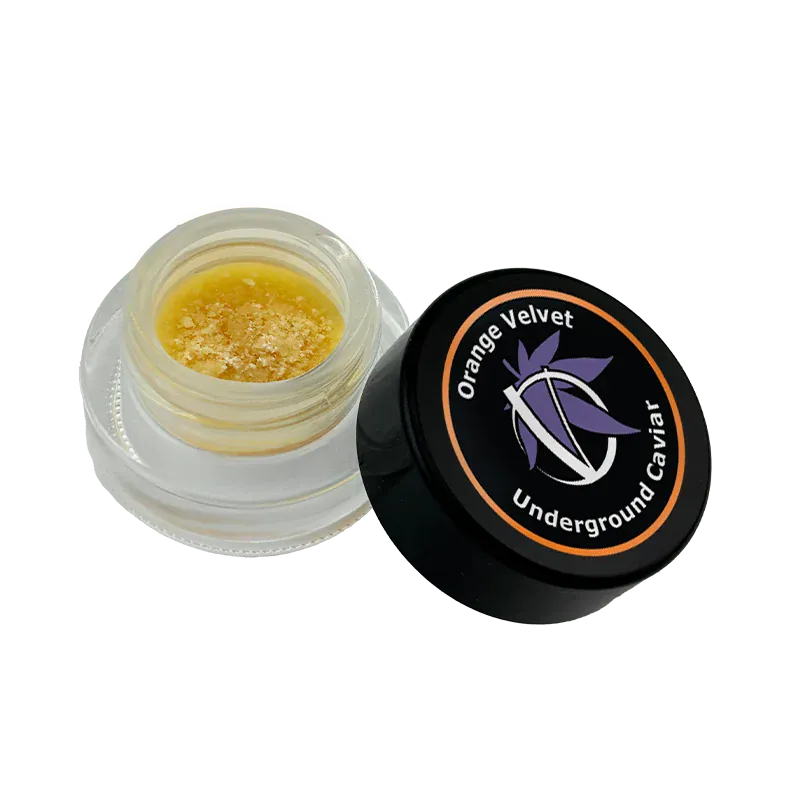 Angled close-up of the open jar of Orange Velvet Underground Caviar showing golden crumbly concentrate and the black lid with the brand logo.