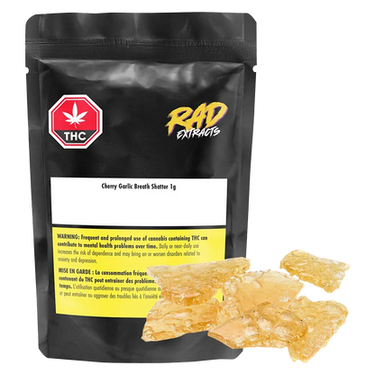 Front-facing shot of a black pouch and amber glassy shards labeled Mango Kush x Galactic Giggles Shatter, the 1 g pieces gleaming against a white background