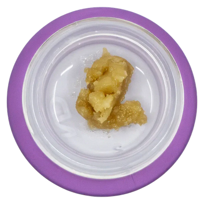 Top-down view of a pale amber concentrate in a white dish with a purple rim labeled Tropical Twist Live Resin Badder.