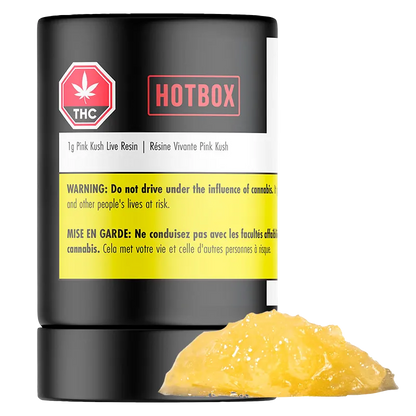 Front-facing shot of a black Hotbox Pink Kush Live Resin container with a yellow warning label and a glossy amber dab of concentrate in front.
