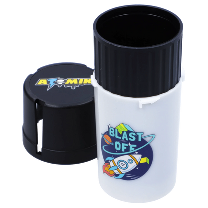 Close-up three-quarter view of the Atomik Grind & Stash showing a white cylindrical body with a rocket "Blast Off" sticker and a removed black grooved cap revealing the hollow interior.