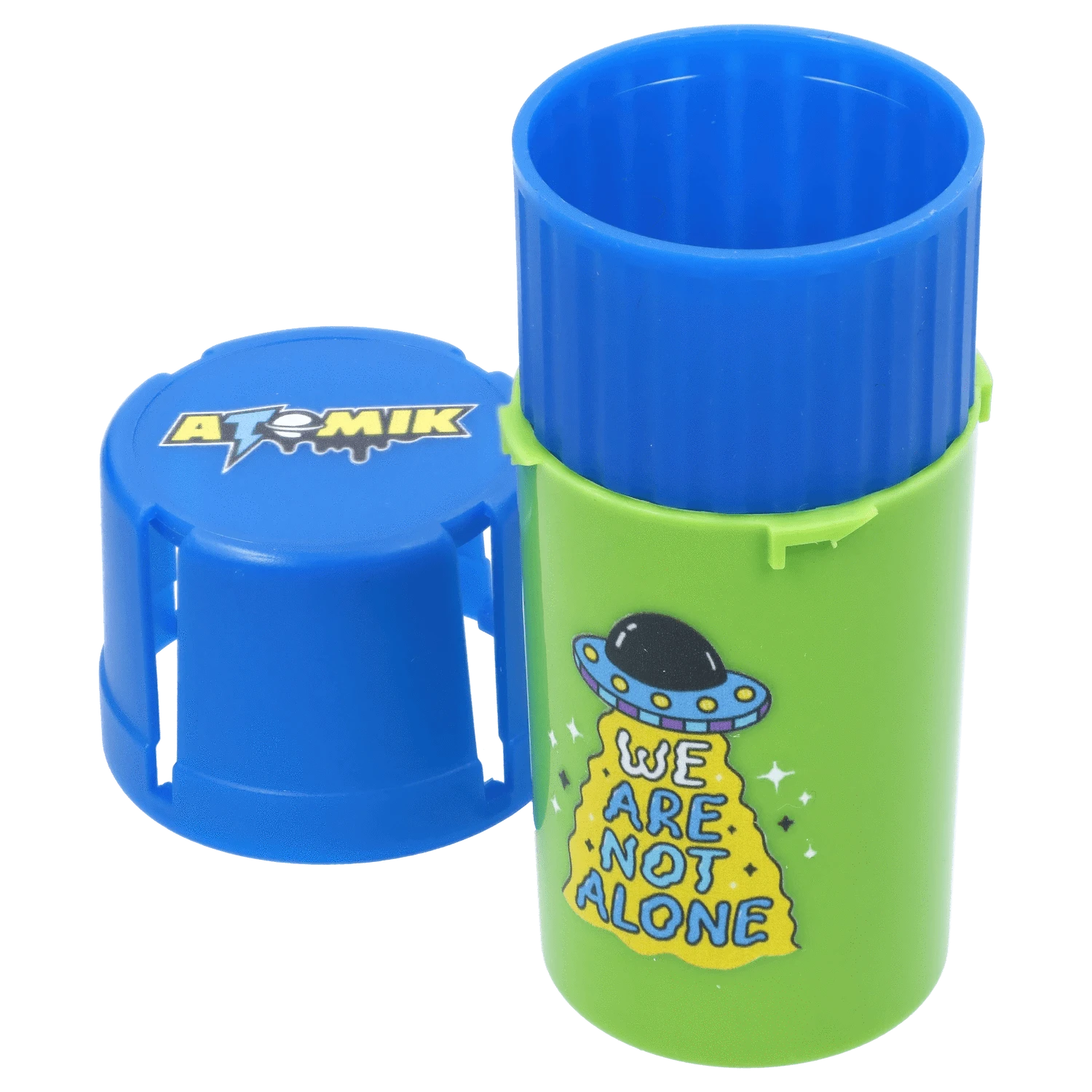 Close-up front view of the green and blue Atomik Grind & Stash tube with its blue lid beside it and a cartoon UFO “We Are Not Alone” graphic.