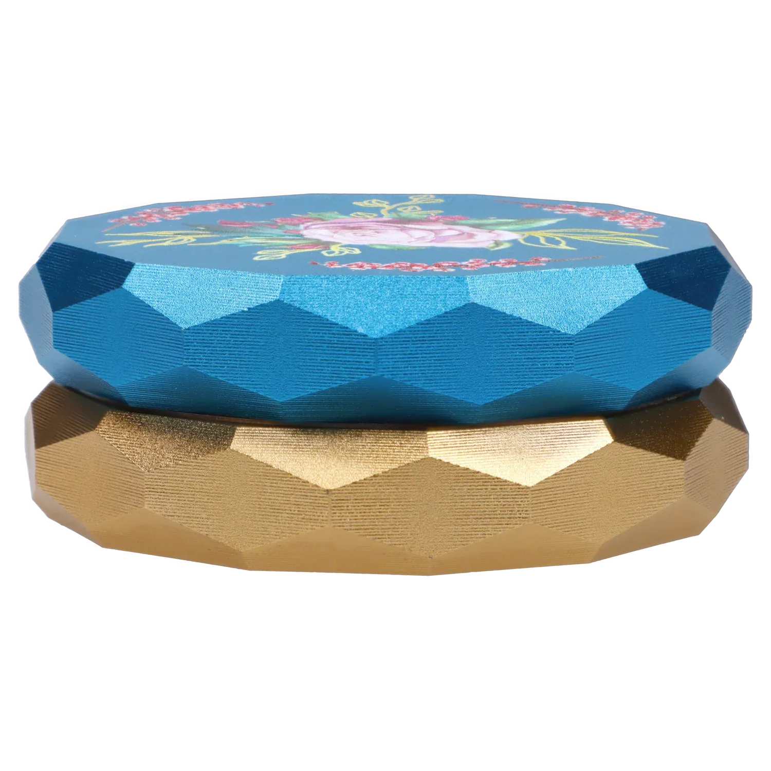 Low-angle close-up of the Famous Design Floral Lush Aluminum 2 Stage Grinder - Teal and Gold showing faceted teal top with floral print over a gold base.