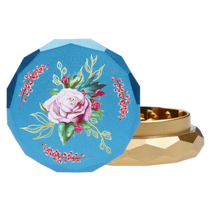 Close-up of the teal lid of the Famous Design Floral Lush Aluminum 2 Stage Grinder - Teal and Gold showing a painted pink rose and gold-accented facets beside the gold lower chamber