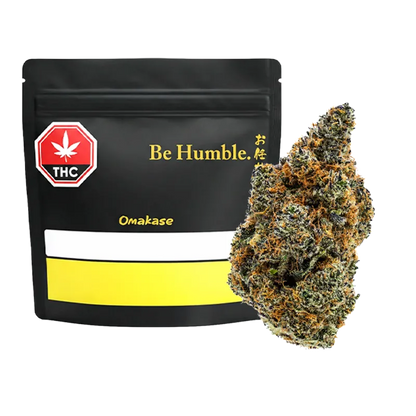 Front view of a black resealable bag labeled "Be Humble. Omakase" beside a close-up of a frosty green and orange bud.