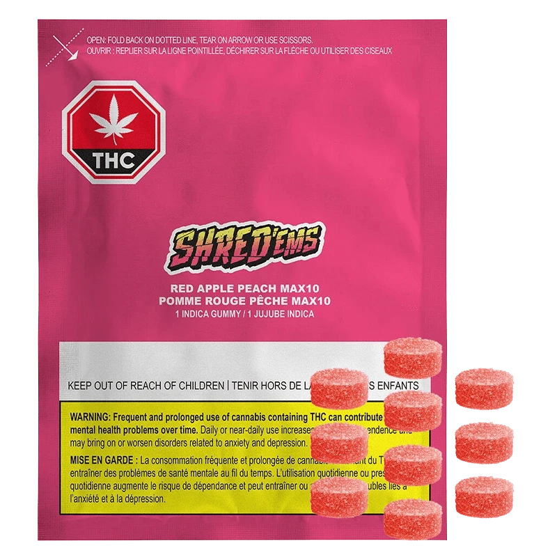 Front-facing shot of the bright pink Shred'ems Red Apple Peach Gummies pouch with warning label at the bottom and several sugar-coated red gummies beside it.