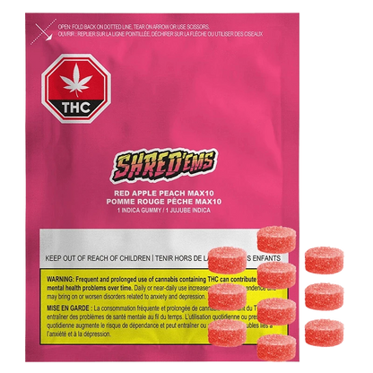 Front-facing shot of the bright pink Shred'ems Red Apple Peach Gummies pouch with warning label at the bottom and several sugar-coated red gummies beside it.