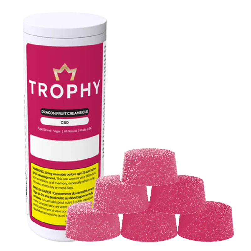 Stacked front view of a white tub labeled Trophy Dragon Fruit Creamsicle Gummies beside six sugar-coated pink gumdrop-shaped candies.