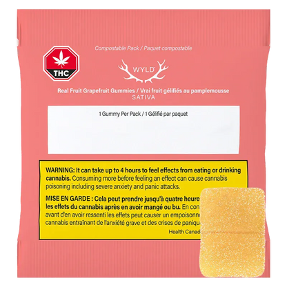 Rear view of the coral packet of Real Fruit Grapefruit Gummies showing a WYLD logo, THC warning badge, yellow bilingual warning box, and a single sugar-coated gummy.