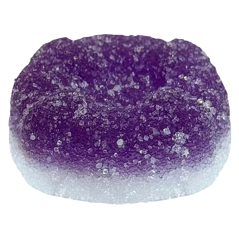 Close-up top view of a sugar-coated purple and white gummy, labeled Ratio'd Moon Berry THC:CBD:CBN Gummies, showing crystalline sugar texture and rounded dome shape.