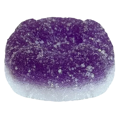 Close-up top view of a sugar-coated purple and white gummy, labeled Ratio'd Moon Berry THC:CBD:CBN Gummies, showing crystalline sugar texture and rounded dome shape.