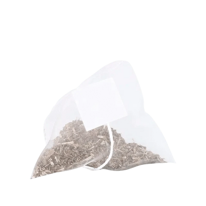 Close-up of a single pyramid tea bag of Decaffeinated Peach Ginger Green Tea Bags filled with loose dried tea and a white tag against a plain white background