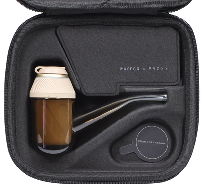 Top-down view of the PUFFCO – Proxy – Desert kit nestled in a black zippered case, showing the tan glass chamber, curved glass mouthpiece, and labeled accessories.
