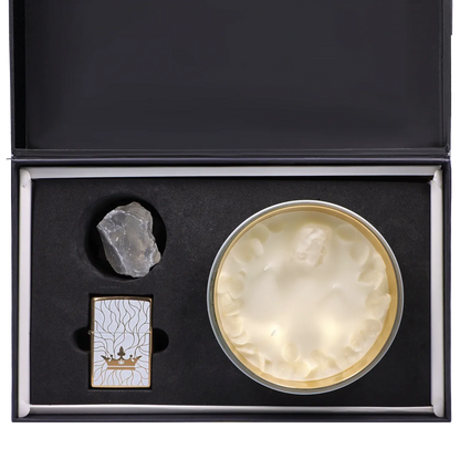 Top-down view of the Queen of Bud: Clarity Ritual Box – Candle, Zippo, and Crystal showing a round white candle in a gold tin, a clear rough crystal, and a patterned gold Zippo nestled in black foam.