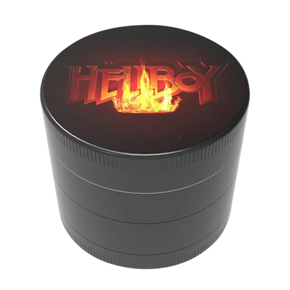 Angled close-up of the Hellboy Logo 3-Stufen Grinder showing its dark circular top with a flaming "HELLBOY" logo centered above the matte black stacked body