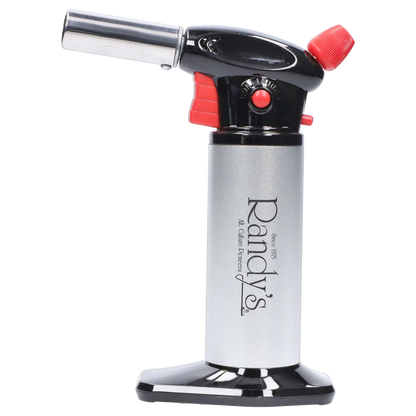 Side profile of Randy's Fahrenheit Butane Torch - Silver showing its chrome nozzle, black and red trigger head, and silver cylindrical body on a reflective black base
