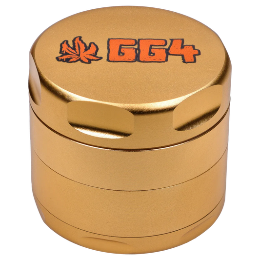 Close-up top-down view of the champagne gold Puff Puff Pass Strains GG4 Grinder-Champagne Gold showing its textured metal finish, recessed grip notches, and orange "GG4" logo with a leaf.