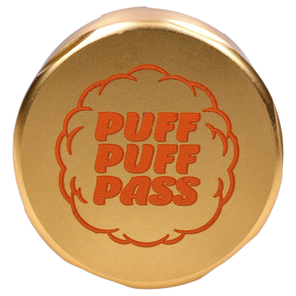 Top-down close-up of the champagne gold Puff Puff Pass Strains GG4 Grinder showing an orange puff-cloud logo and bold "PUFF PUFF PASS" text.