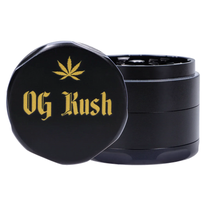 Close-up front three-quarter view of the black Puff Puff Pass Strains OG Kush Grinder-Black with gold "OG Kush" text and a gold leaf emblem on the lid.